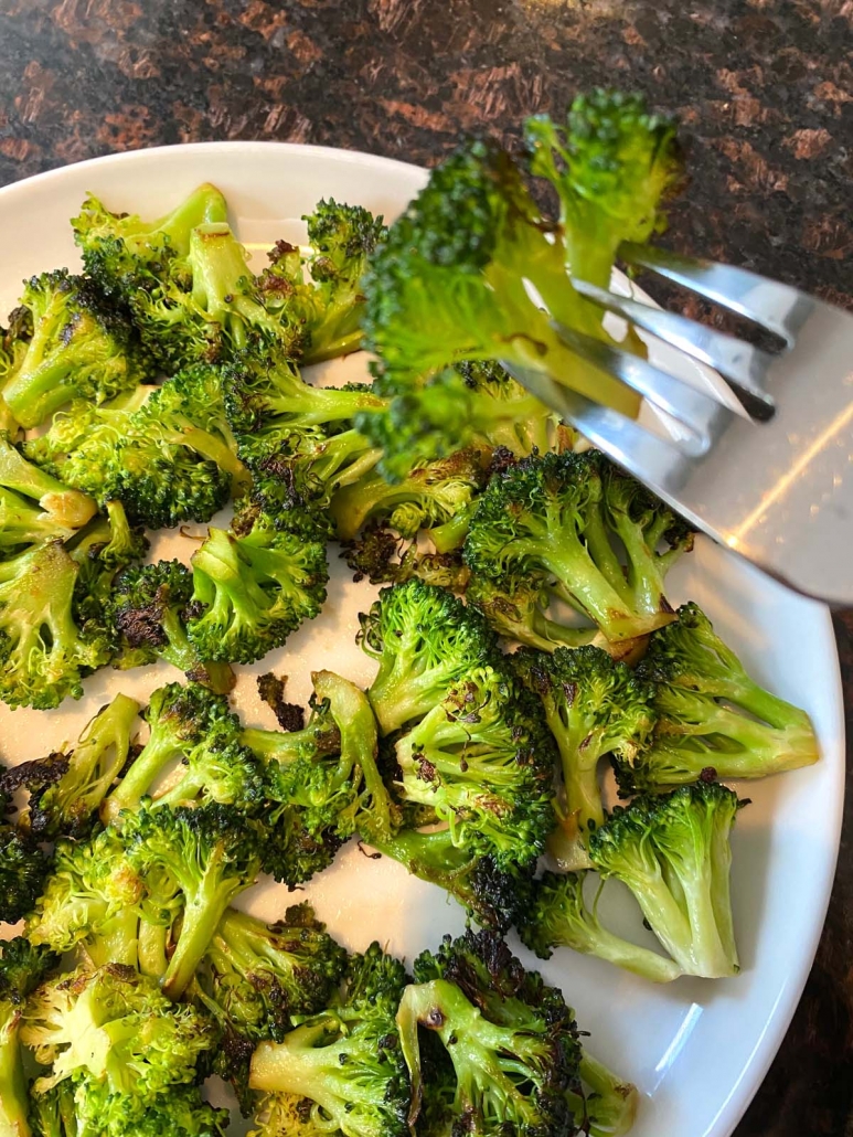 fork holding broccoli above plate filled with broccoli