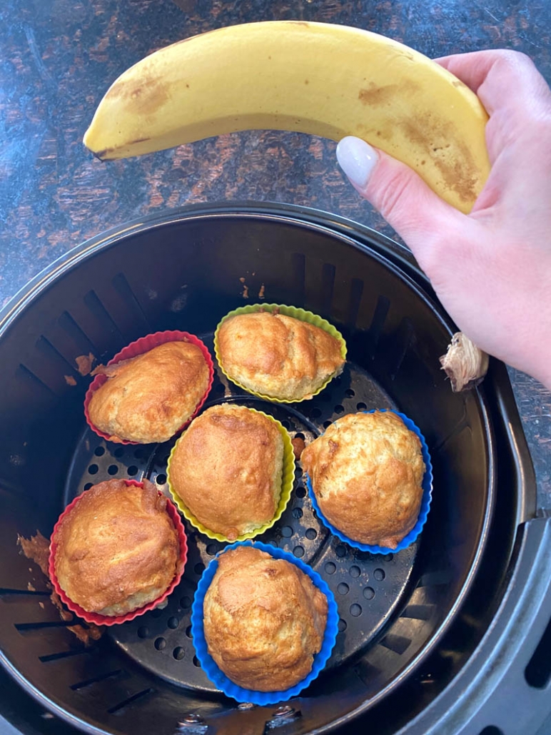 hand holding a banana above air fryer with muffins inside
