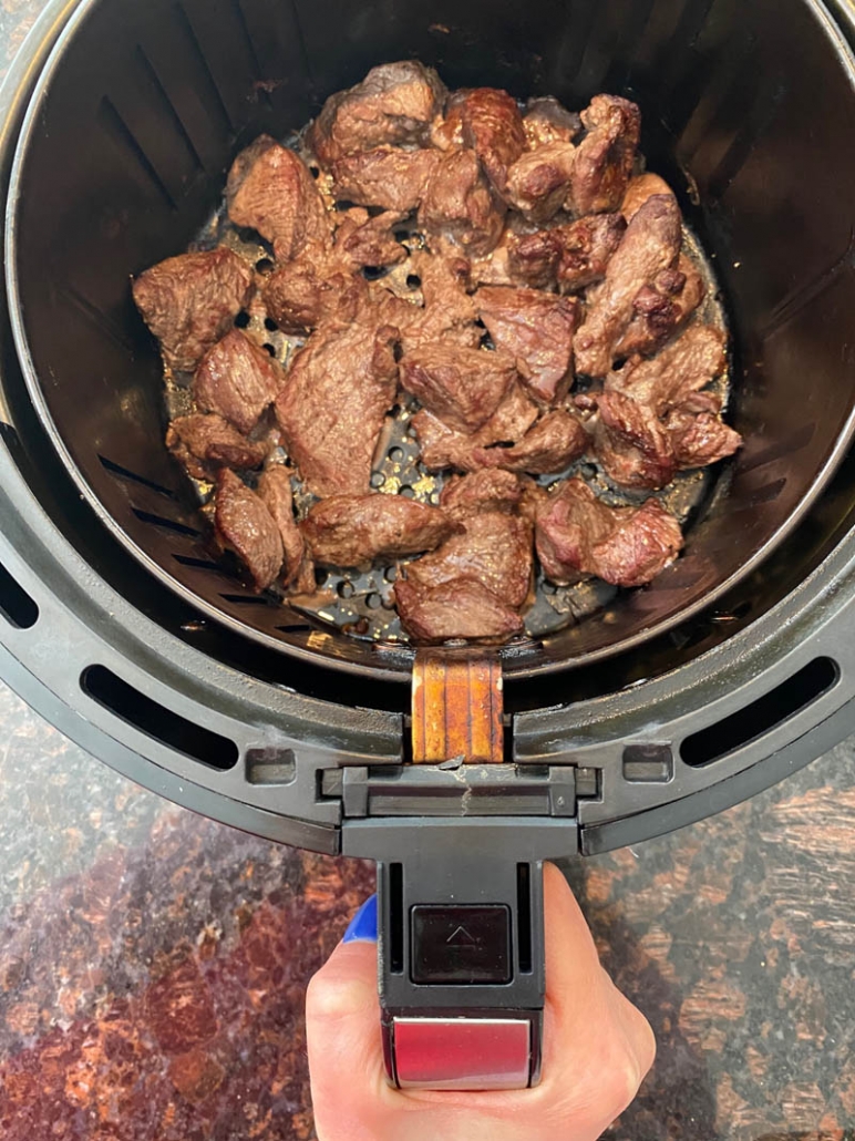 hand holding air fryer basket with small pieces of steak inside