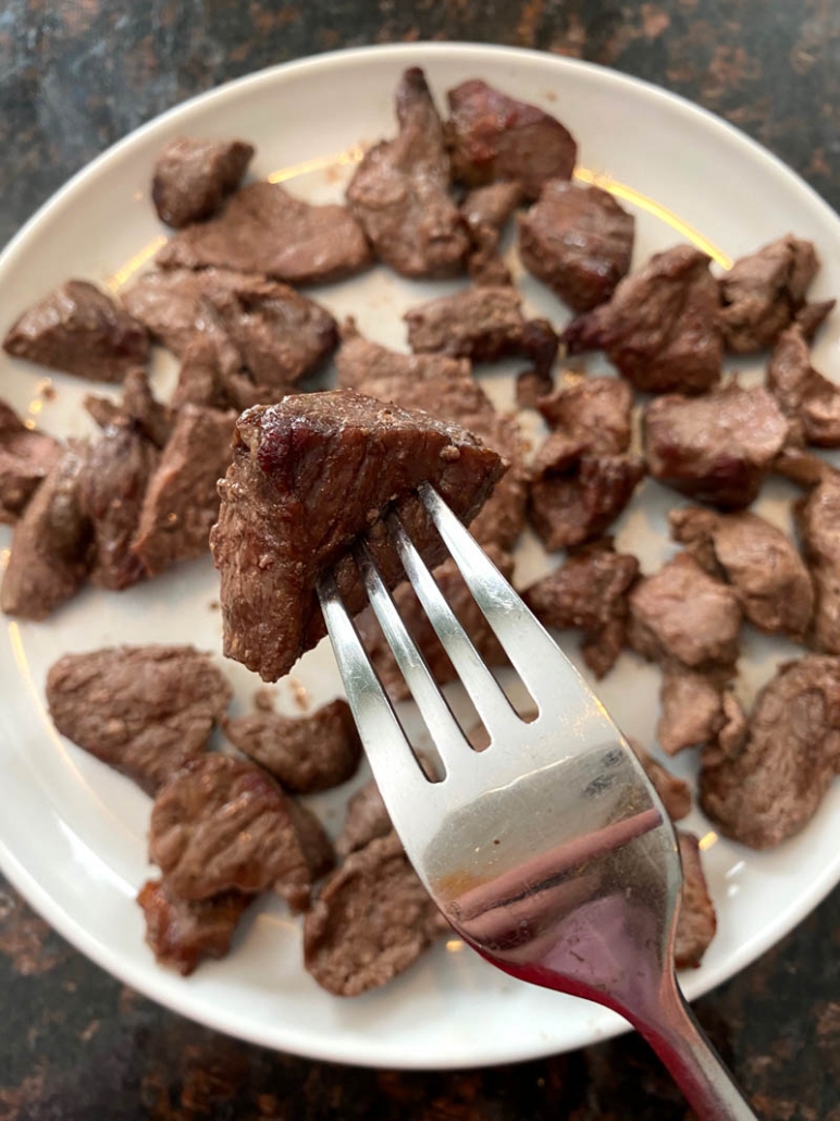 fork holding steak bite air fried above plate of bites