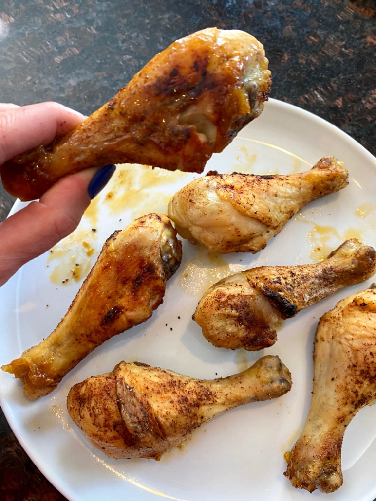 hand holding oven baked chicken drumstick above plate of drumsticks