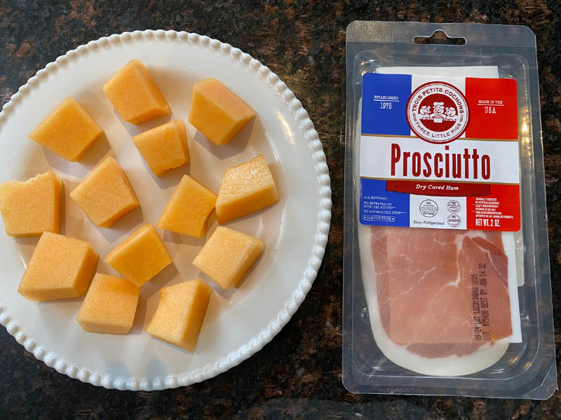 Cantaloupe pieces on a plate and a package of prosciutto. 