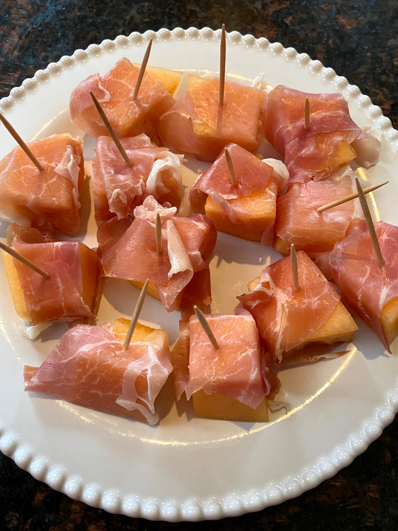 Prosciutto wrapped cantaloupe on a plate.