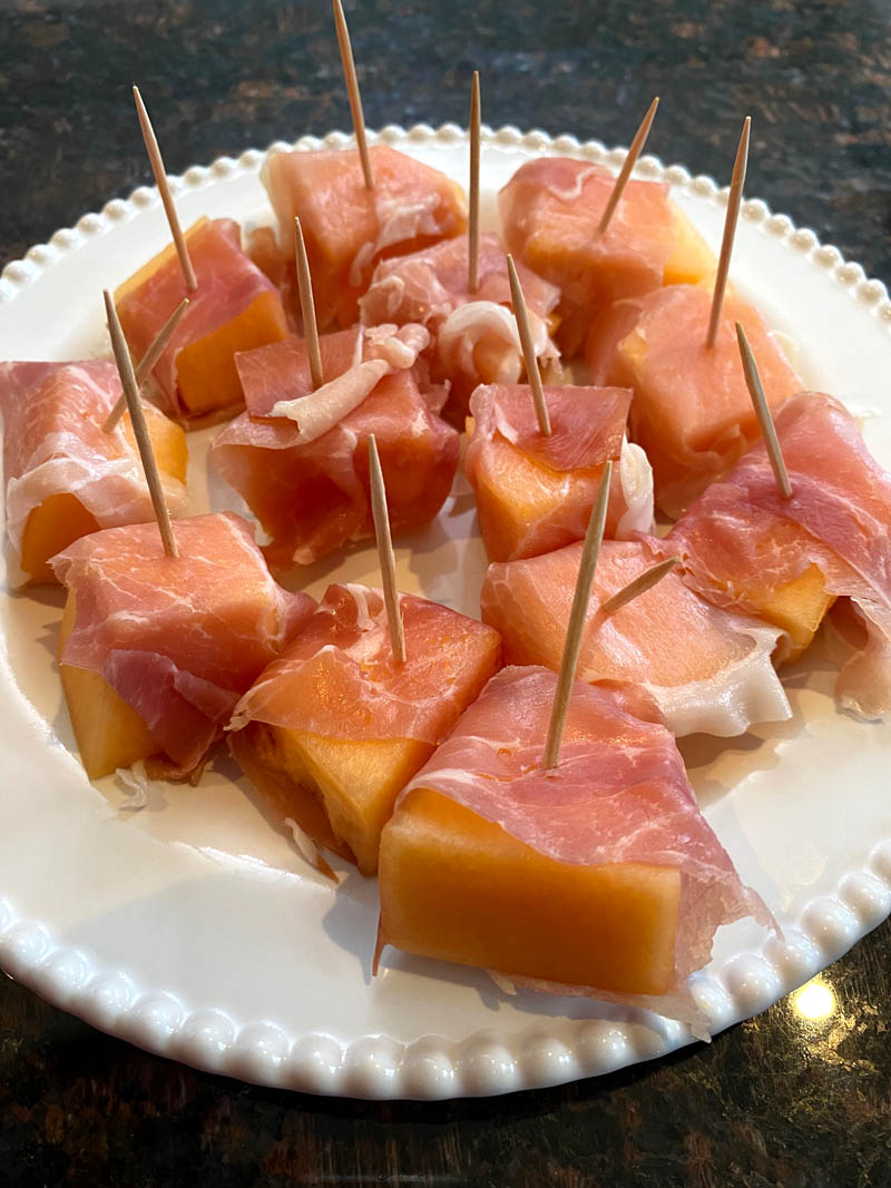 Prosciutto wrapped cantaloupe on a plate.