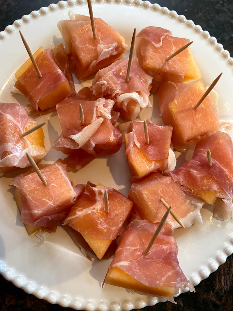 Prosciutto wrapped cantaloupe on a plate.