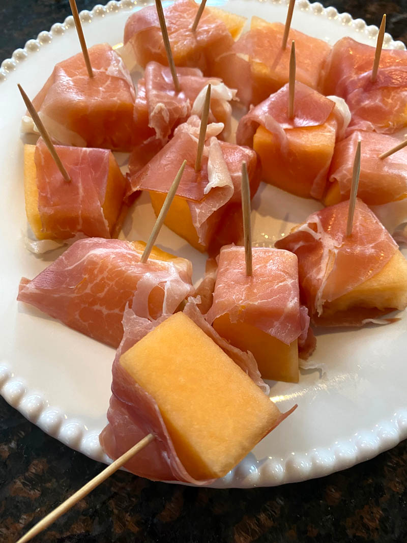 Prosciutto wrapped cantaloupe on a plate.