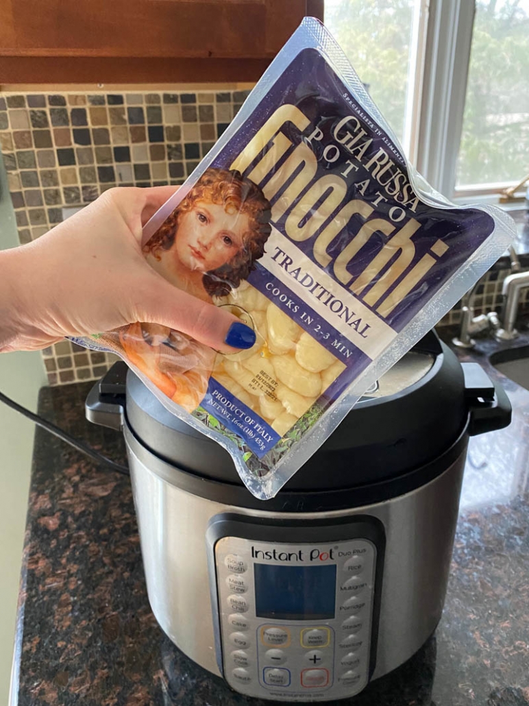 hand holding package of gnocchi in front of the instant pot