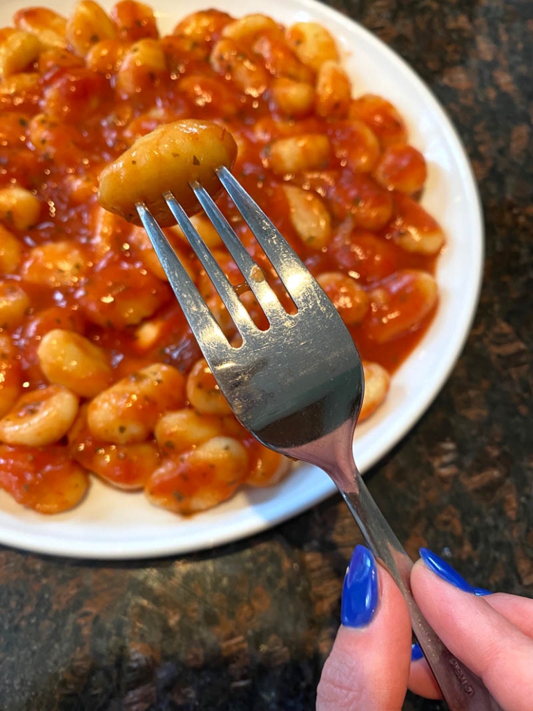 fork picking up gnocchi from a plate of gnocchi in tomato sauce