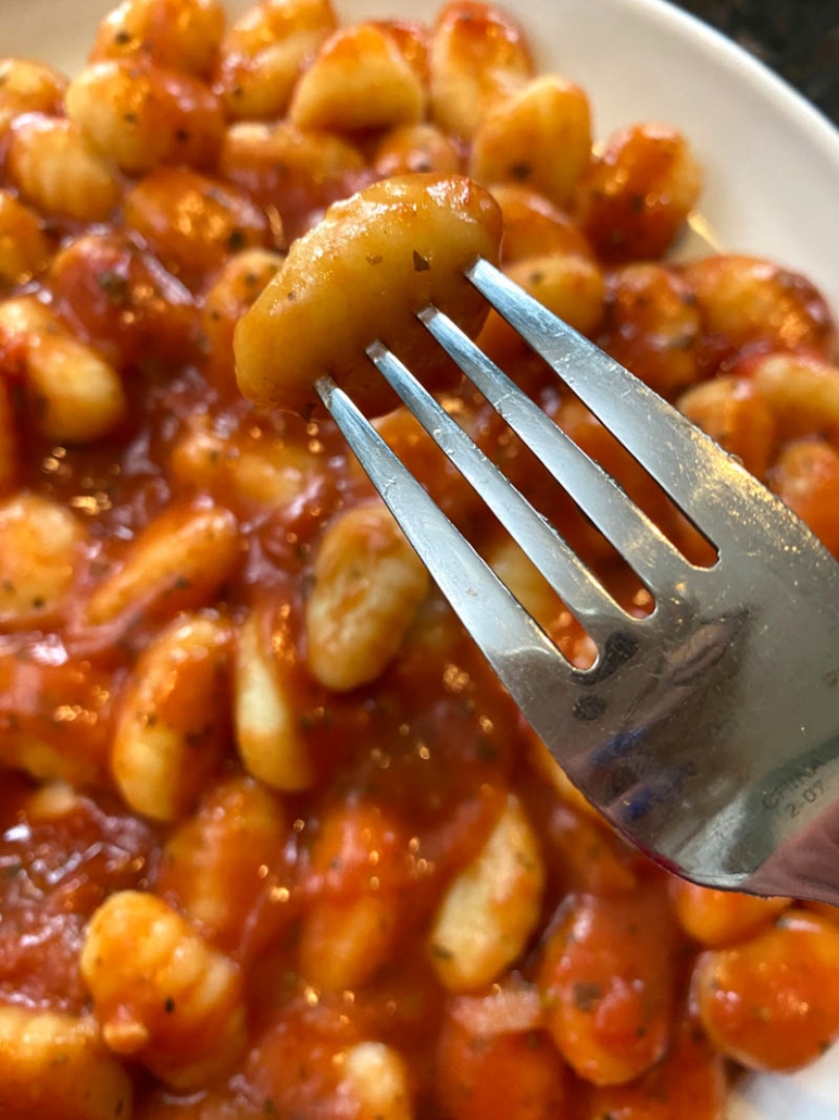 close up of fork holding gnocchi above plate filled with instant pot cooked gnocchi in tomato sauce