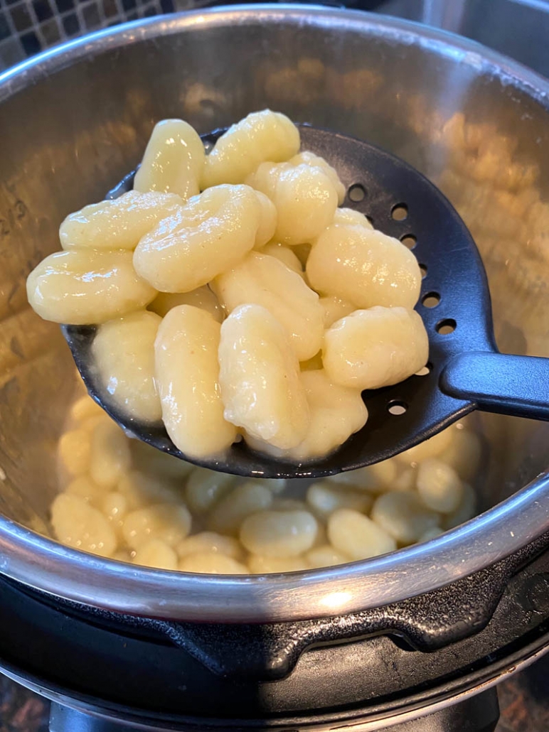 slotted spoon straining gnocchi above instant pot