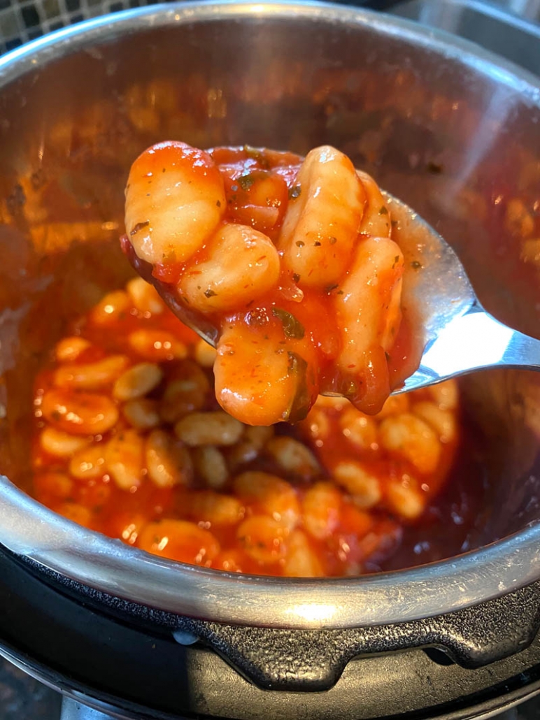 spoon holding cooked gnocchi in tomato sauce above instant pot filled with gnocchi
