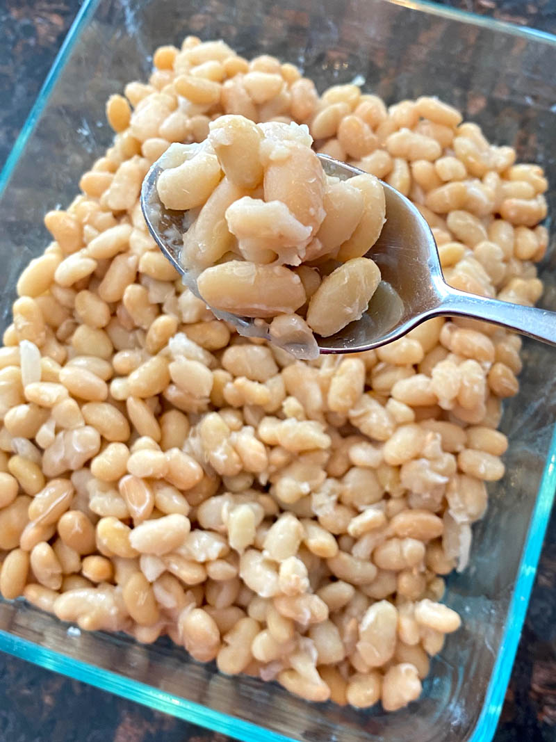 Cooked great northern beans in a dish with a spoon of them.
