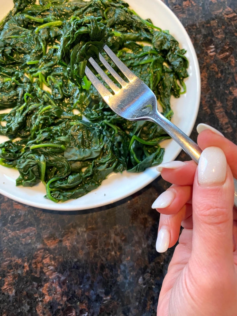 hand holding fork above plate filled with spinach