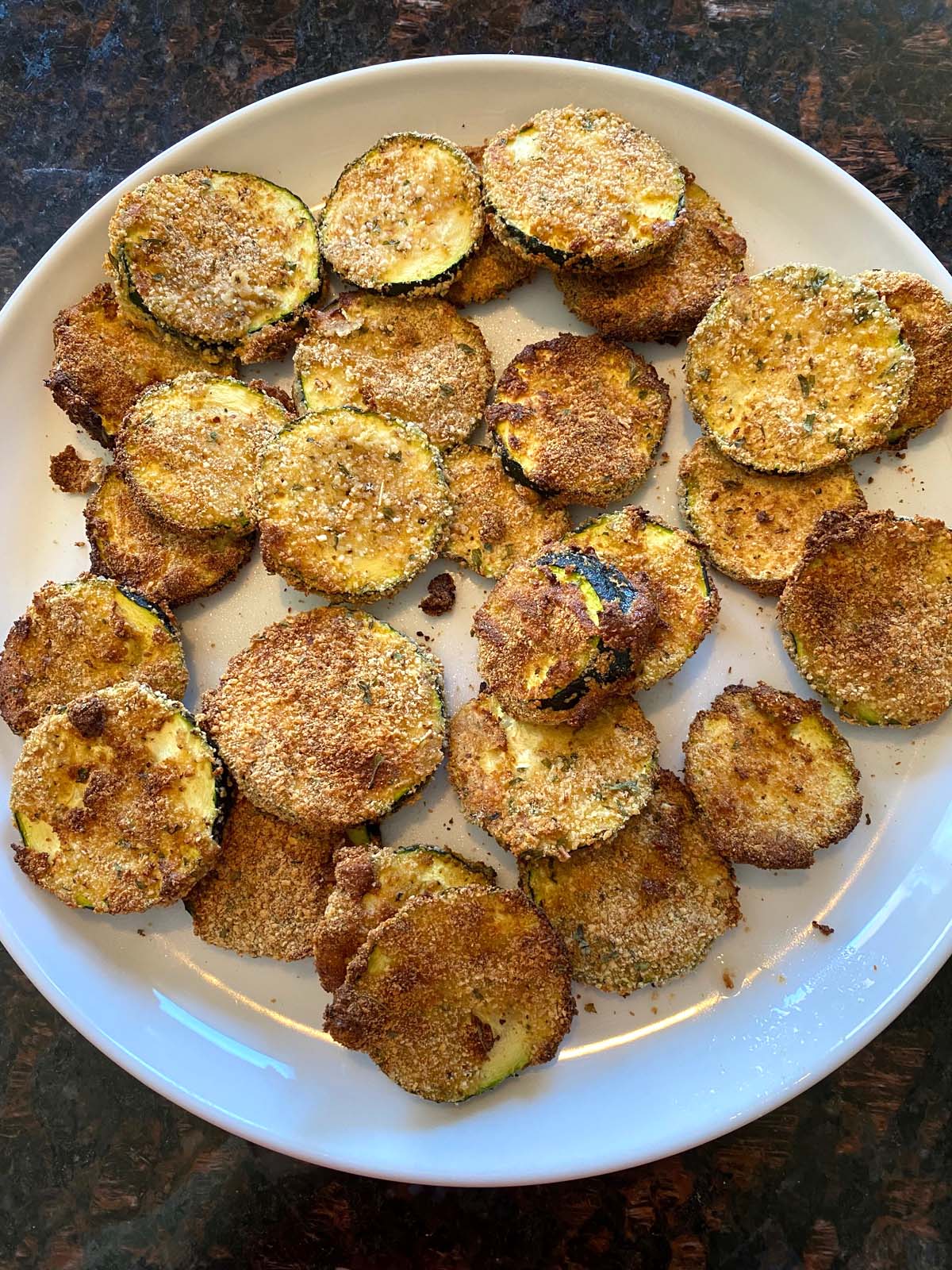 Breaded air fried zucchini chips on a white plate.