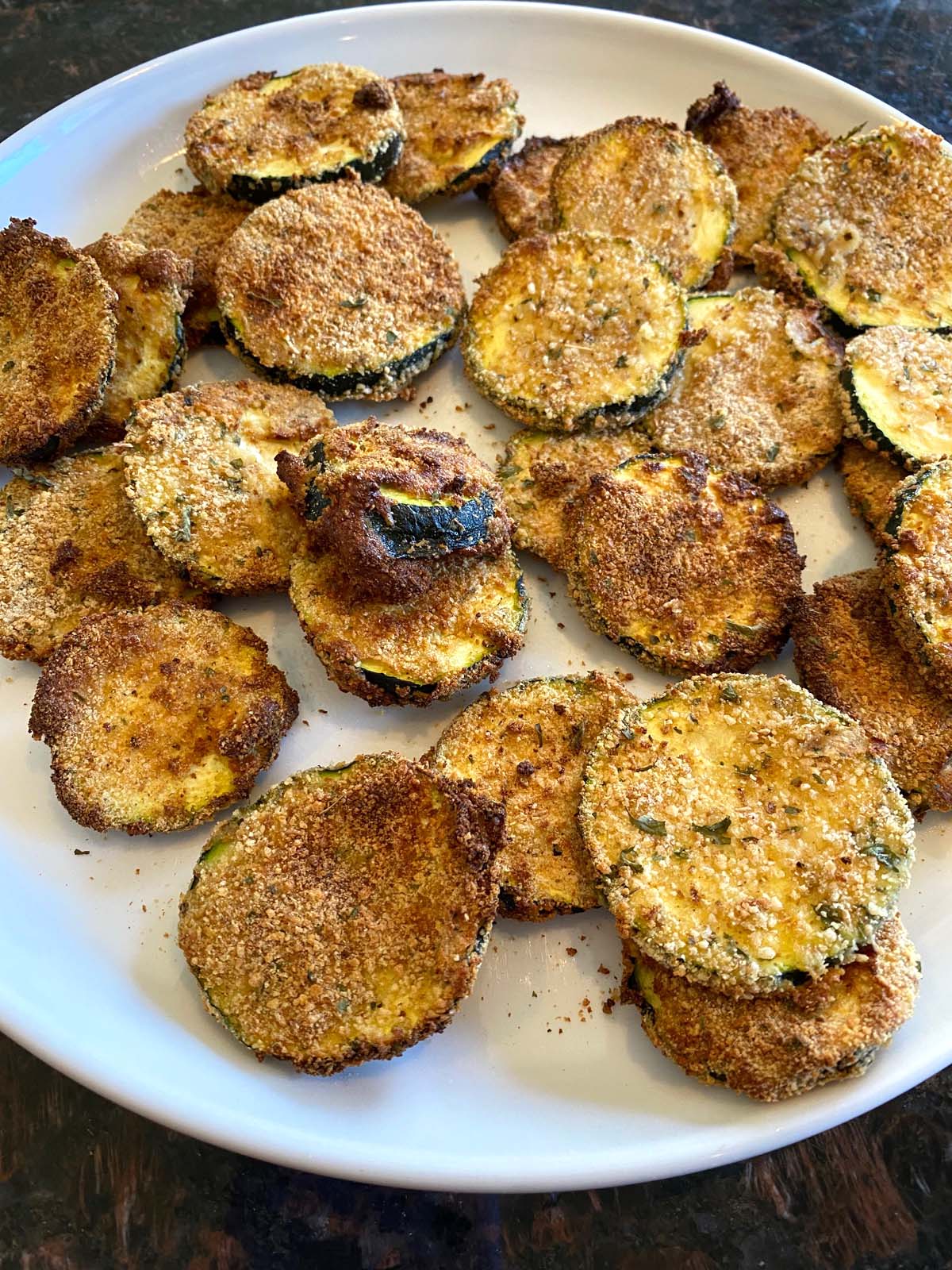 Breaded air fried zucchini chips on a white plate.