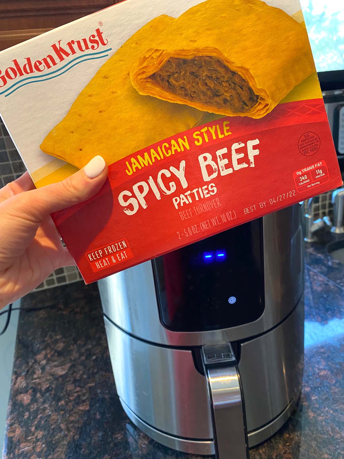 A package of Jamaican beef patties being held in up in front of an air fryer with the box next to it.