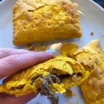 Cooked Jamaican beef patties on a plate with one half being held up.