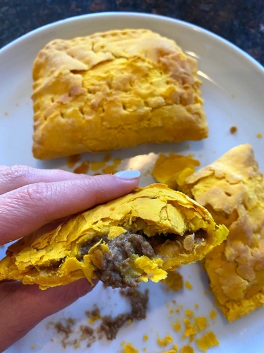 Cooked Jamaican beef patties on a plate with one half being held up.