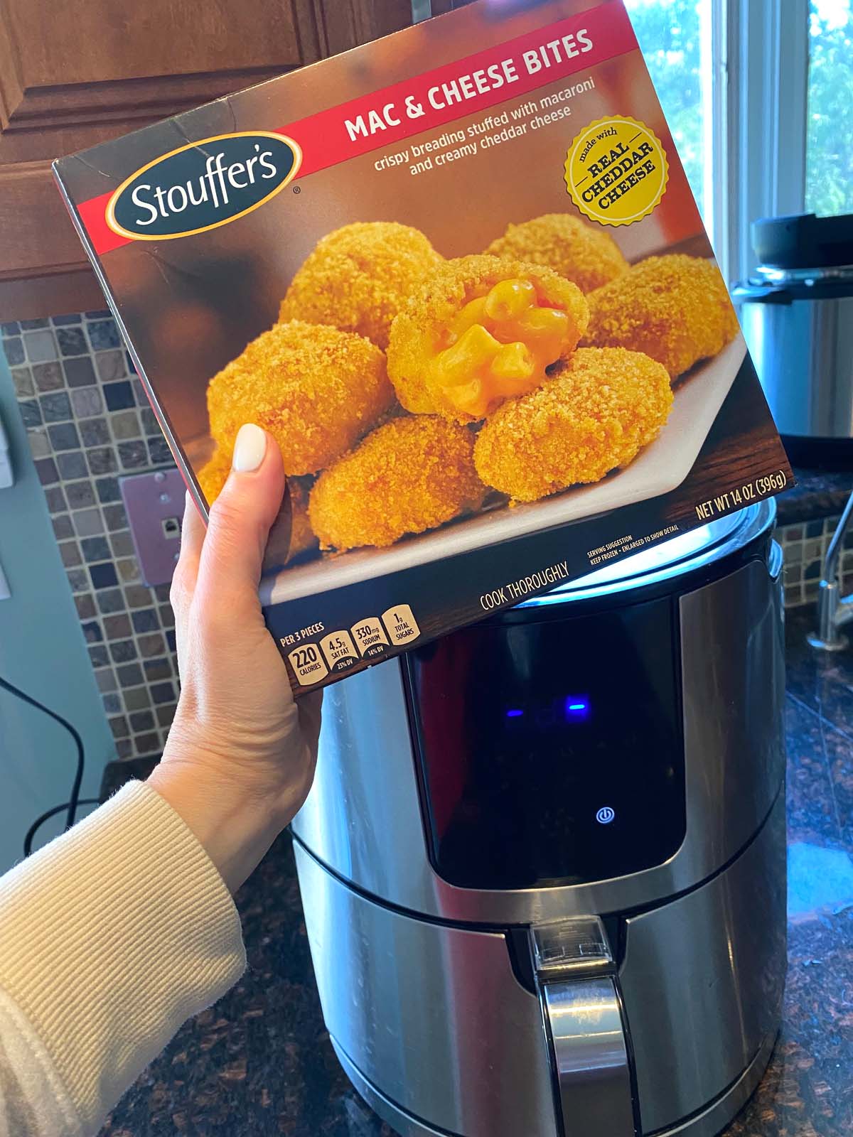 A box of mac and cheese bites being held up in front of an air fryer.