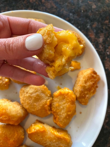 Cooked mac and cheese bites on a plate with one being held up.