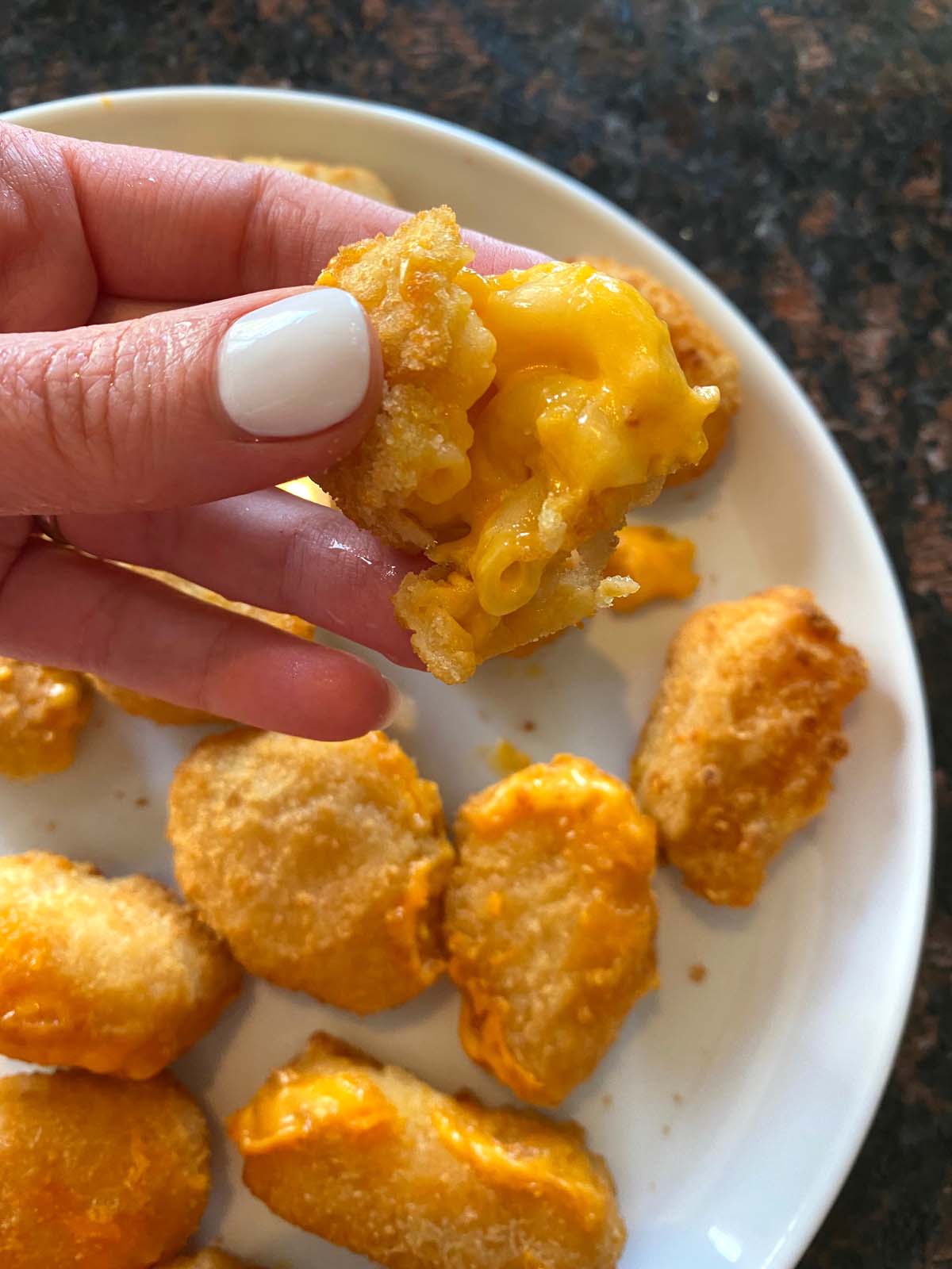 Cooked mac and cheese bites on a plate with one being held up.