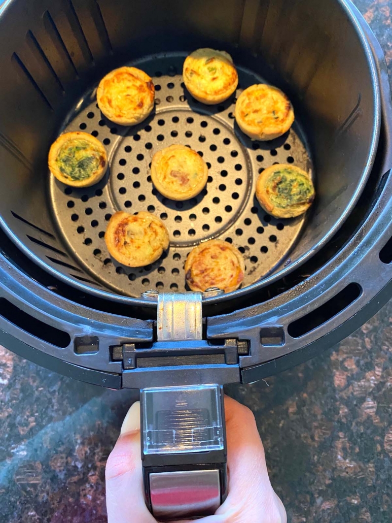 hand pulling out air fryer basket with mini quiches