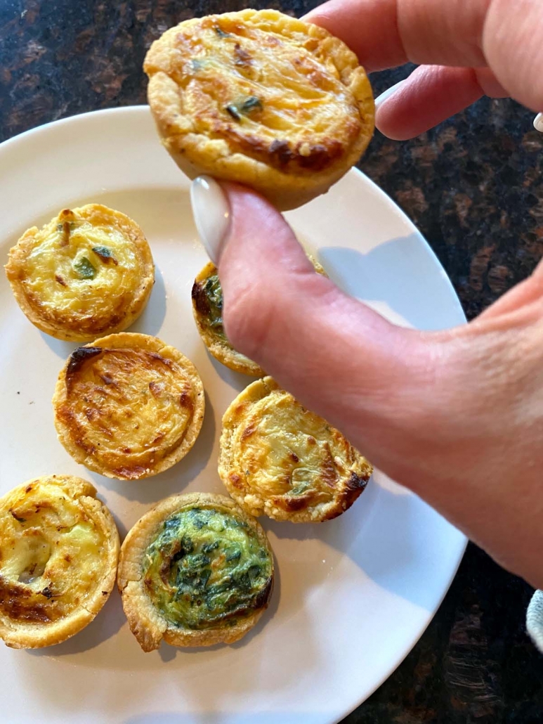 hand holding air fried mini quiche above a plate of mini quiches