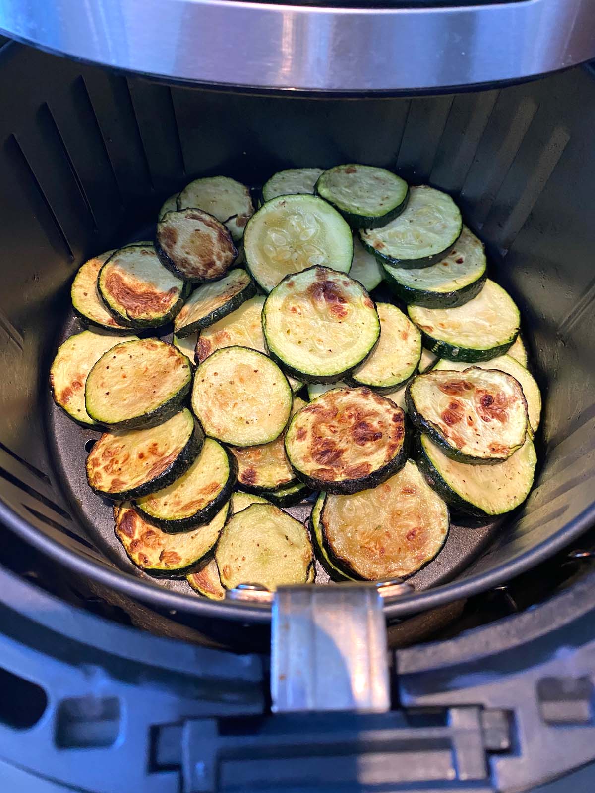 Air fryer roasted zucchini slices in the air fryer basket.