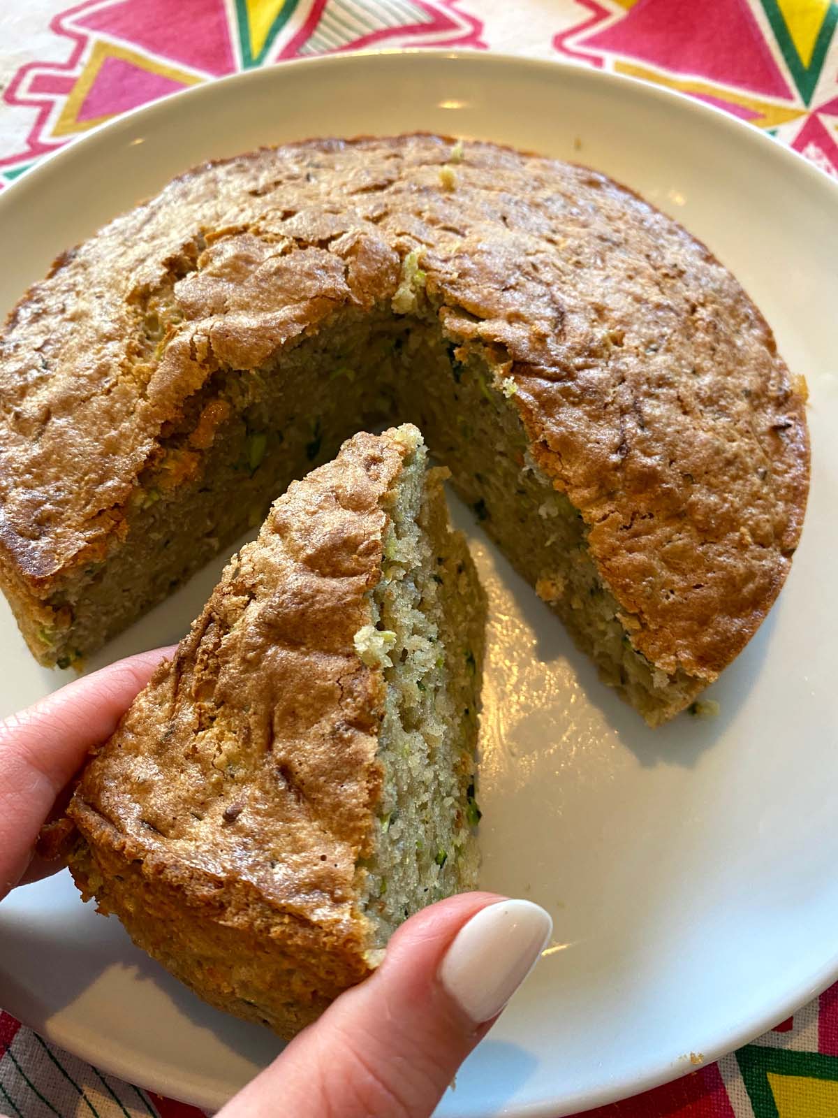 Air fryer zucchini bread on a white plate with a slice being held up.