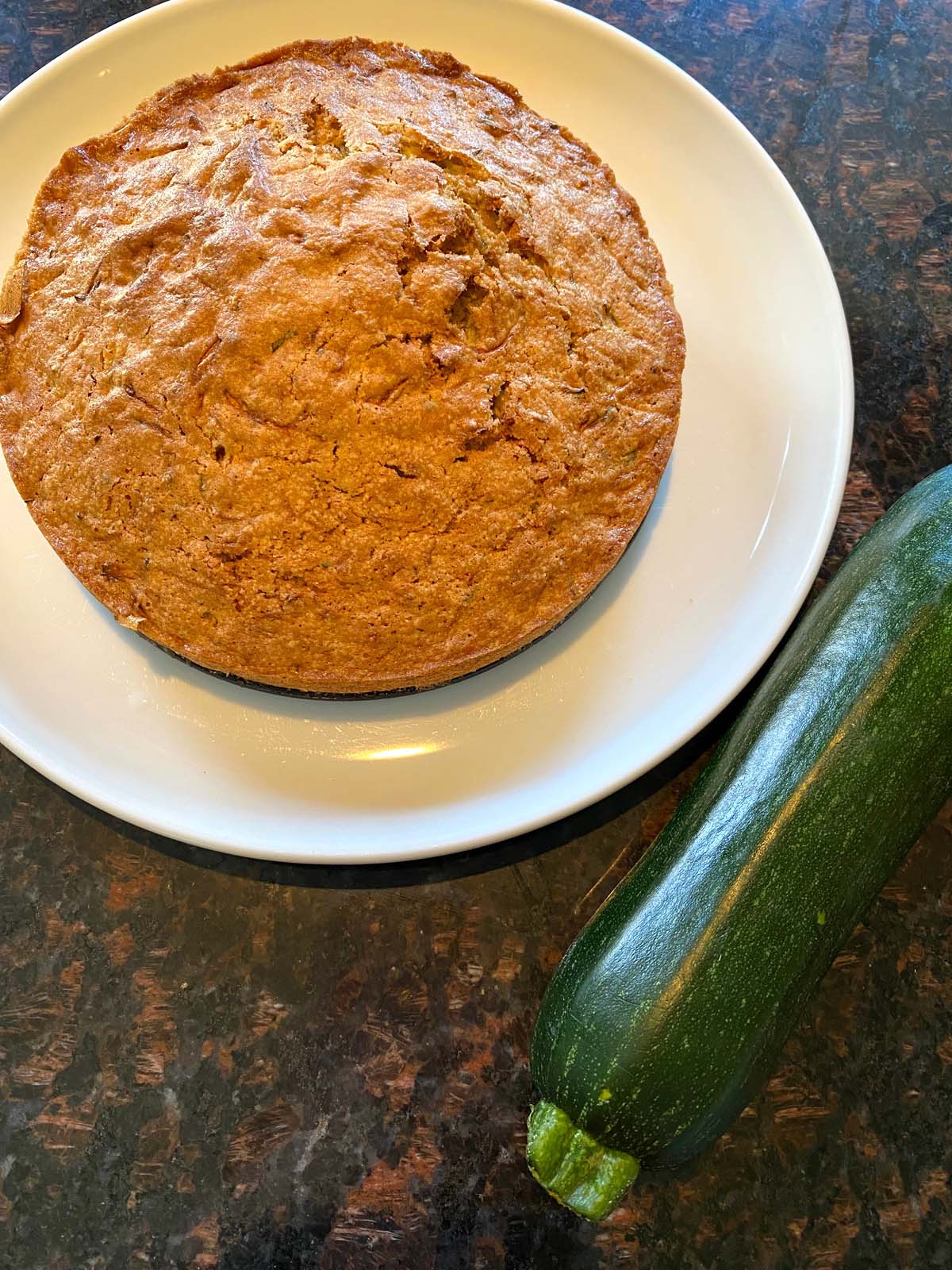 A baked air fryer zucchini bread on a white plate with a raw zucchini next to it.
