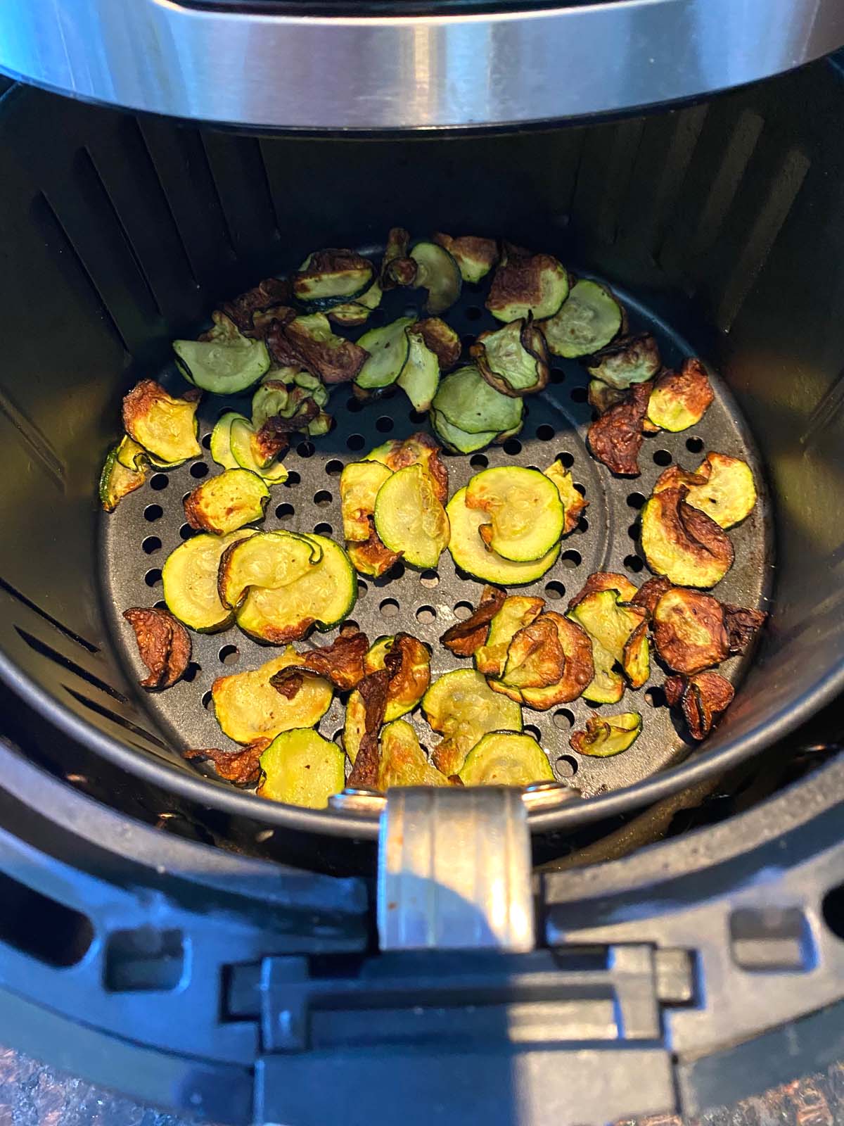 Air fryer basket with zucchini chips.