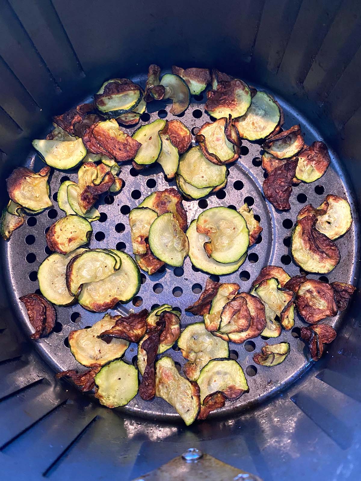 Close up of zucchini chips in air fryer basket.