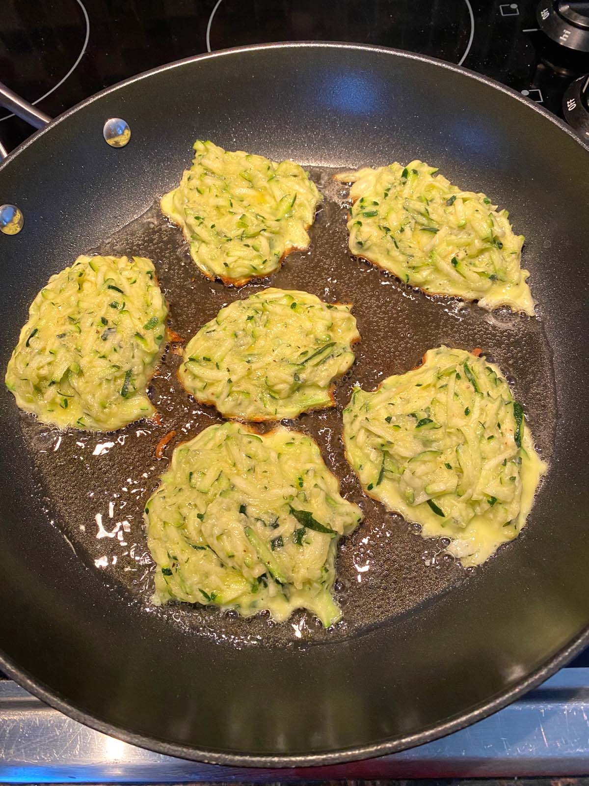 Zucchini pancakes being cooked in a frying pan.