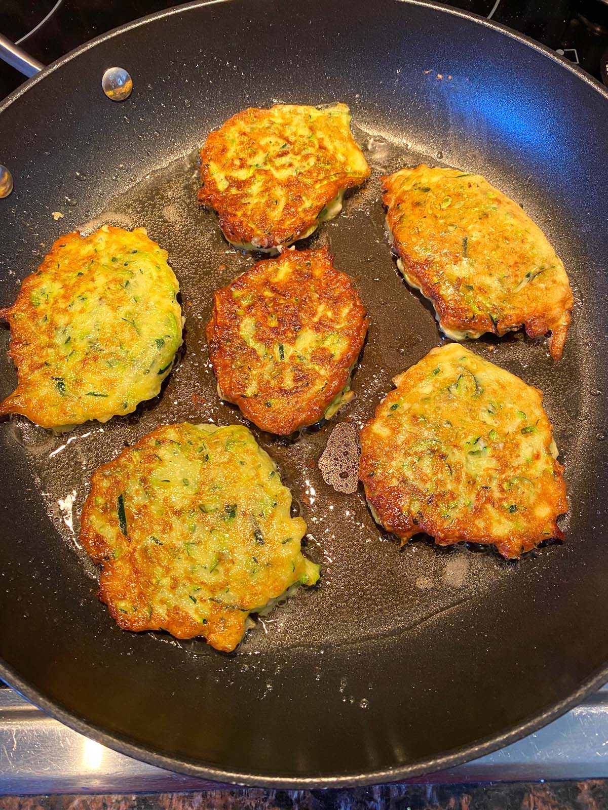 Zucchini pancakes being cooked in a frying pan.