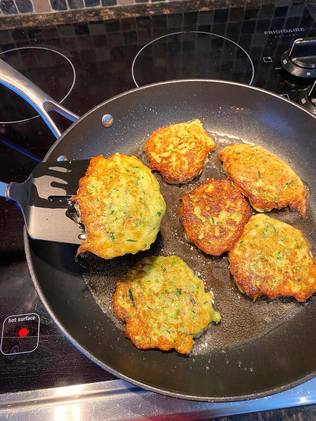 Zucchini pancakes being cooked in a frying pan.