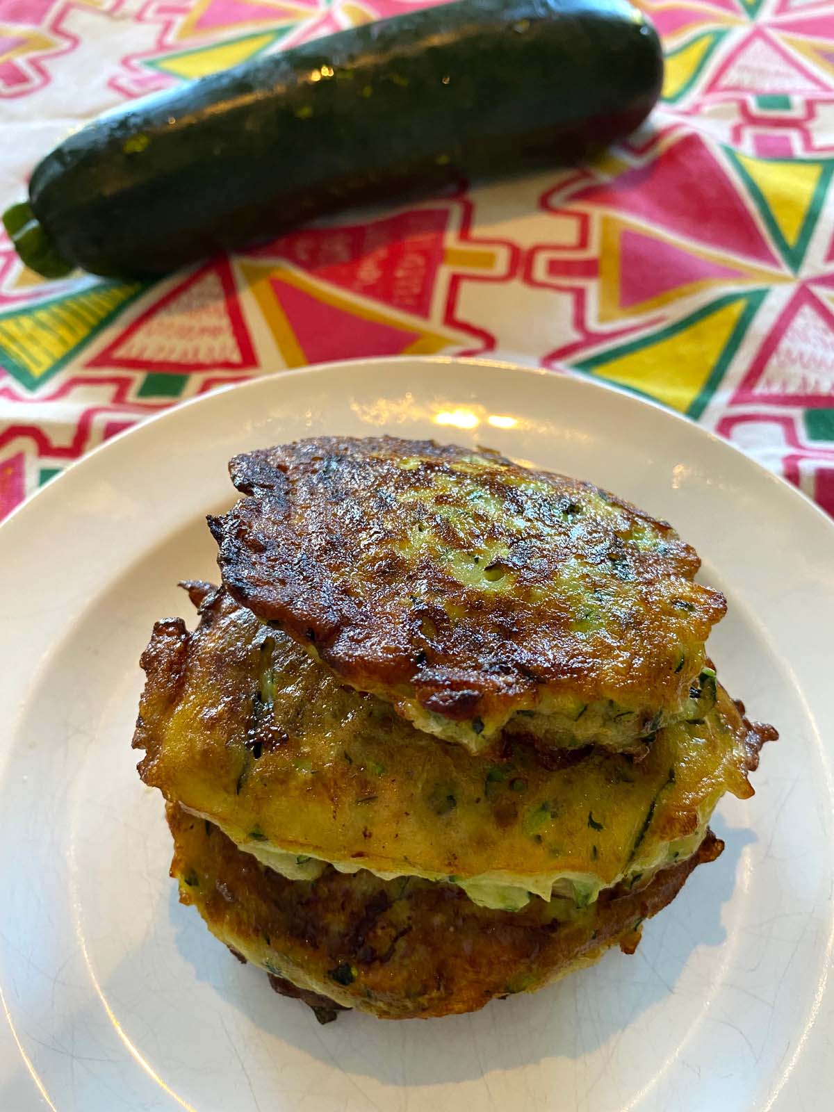 Zucchini pancakes on a plate with a raw zucchini on the side.