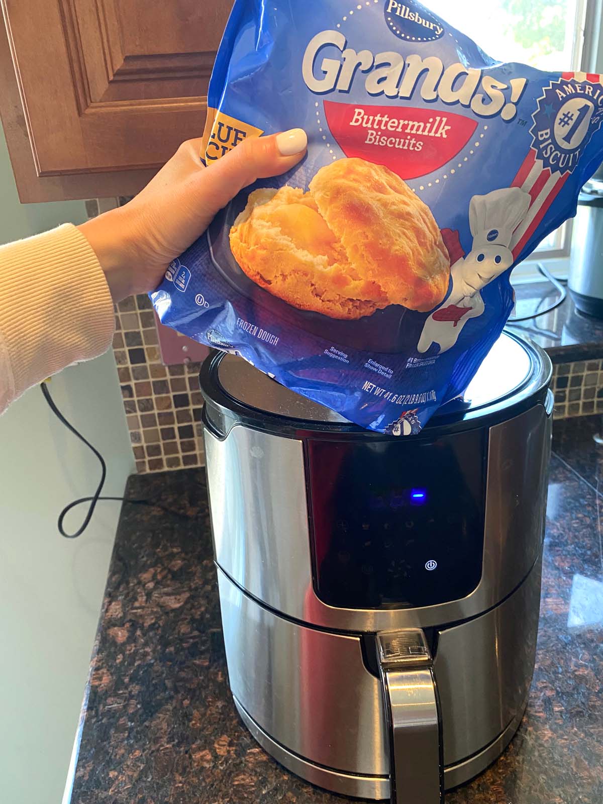 Package of Grands frozen biscuits being held up in front of an air fryer.