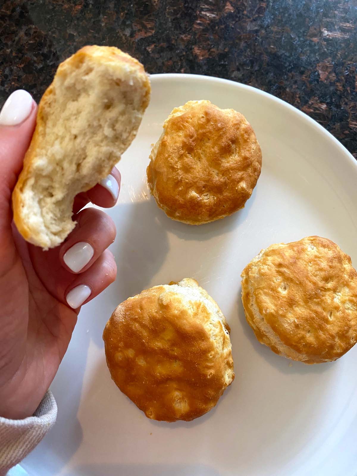 Cooked biscuits on a plate with one being held up.