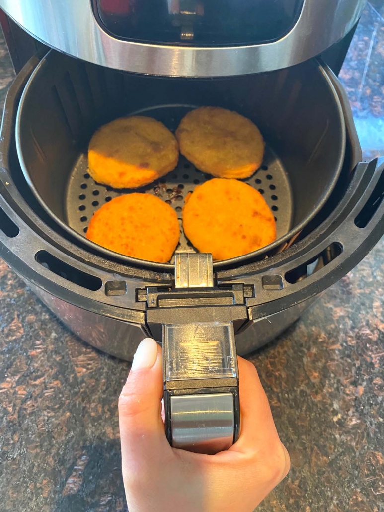 hand opening air fryer to show cooked breaded chicken patties