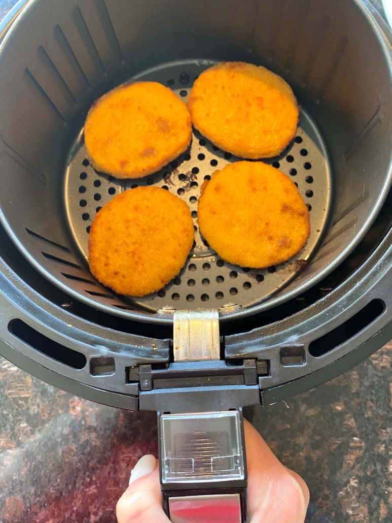 hand holding air fryer basket with breaded chicken patties inside