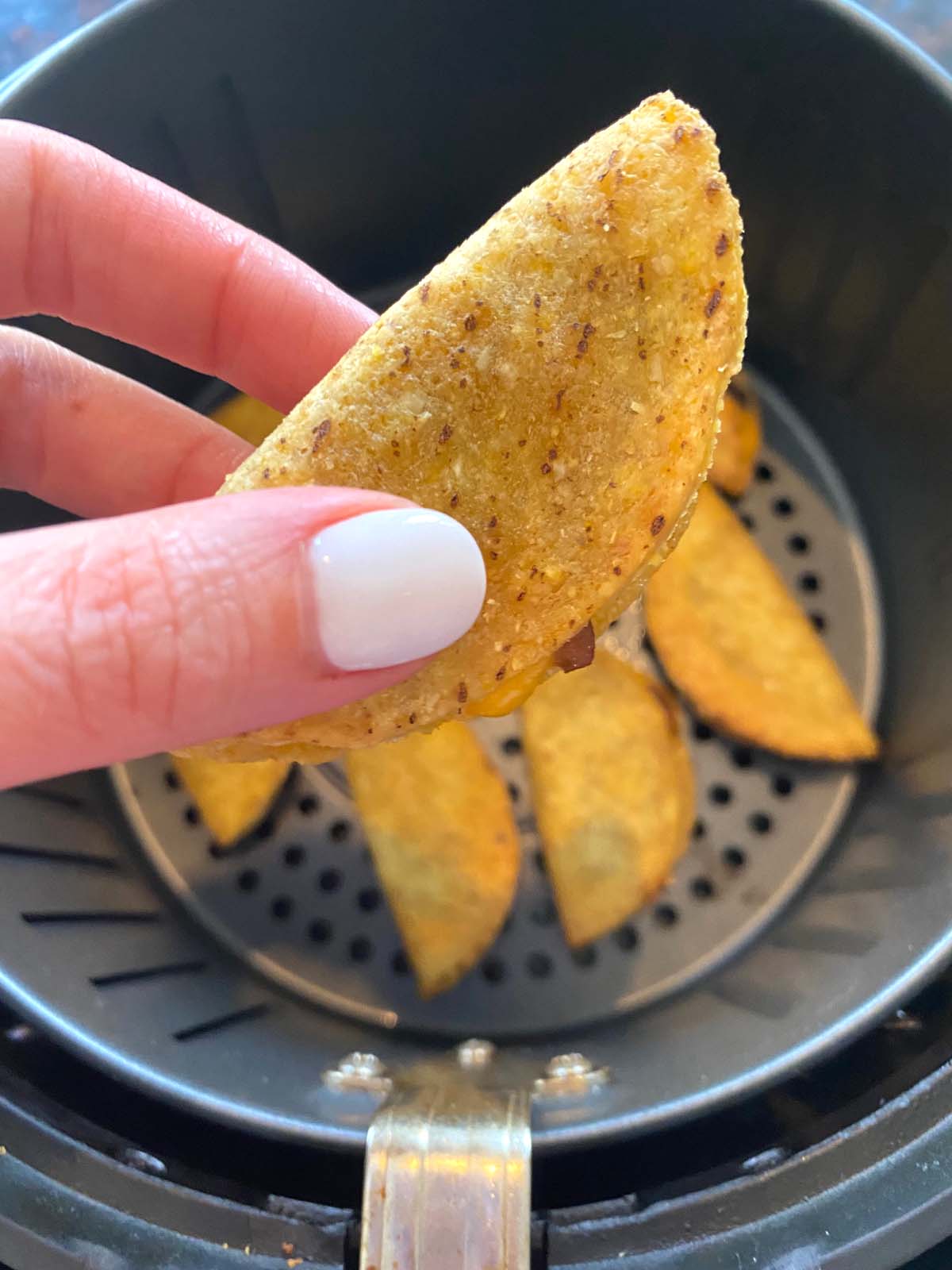Hand holding a mini taco close up with basket of more underneath.