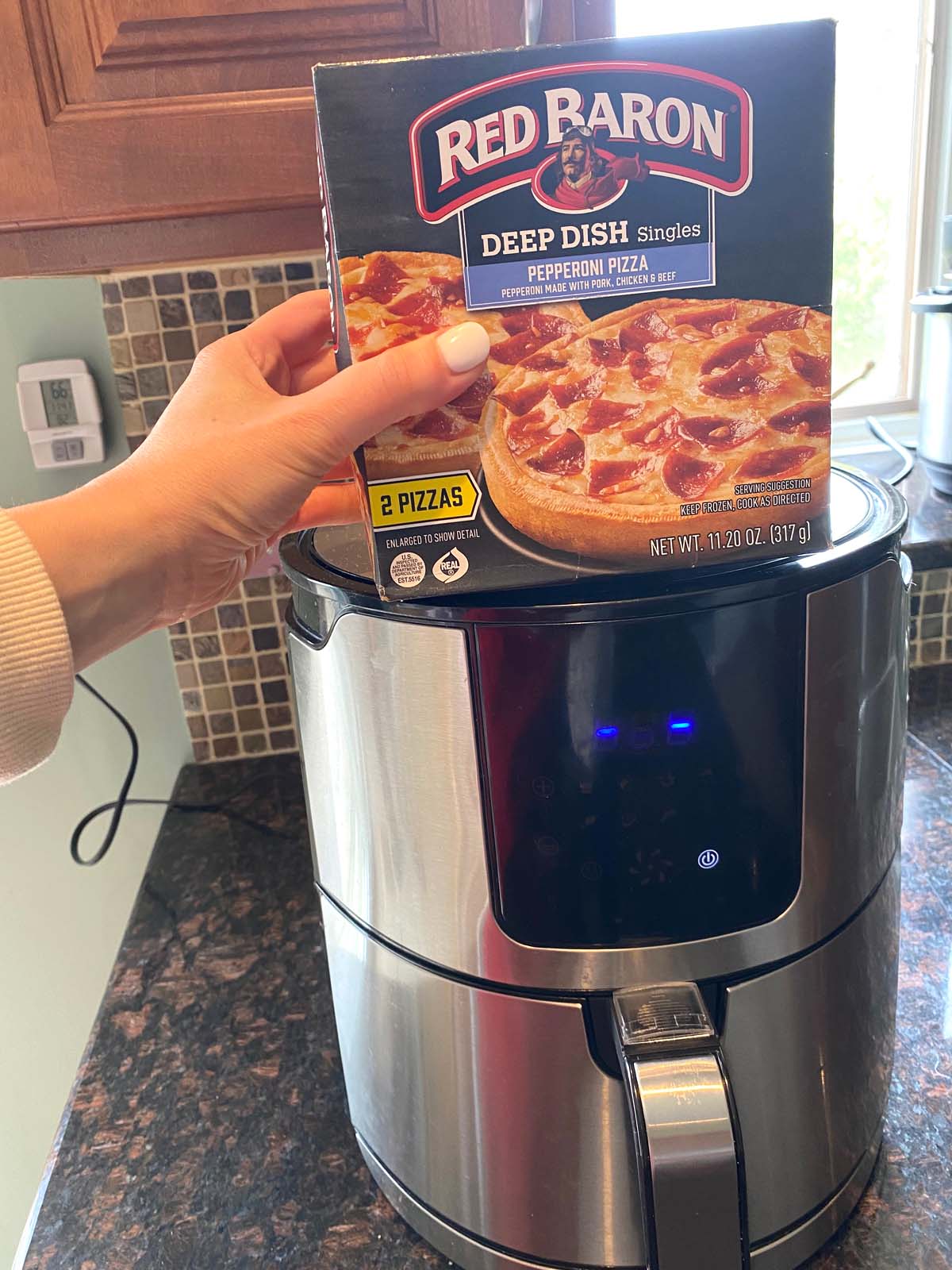A box of Red Baron Deep dish singles pepperoni pizza being shown over an air fryer.
