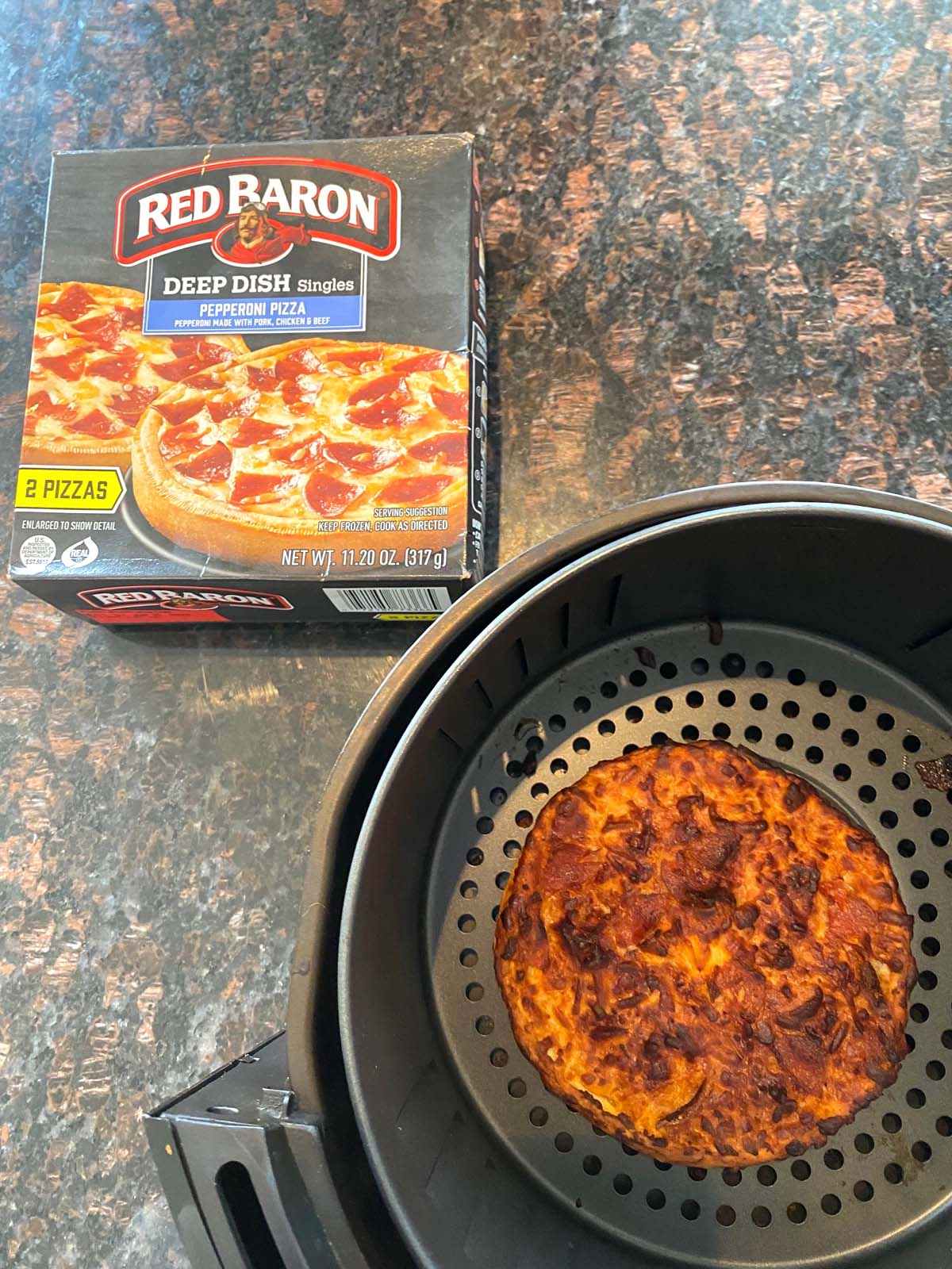 Box of red baron frozen pizza next to air fryer basket with cooked pizza inside.
