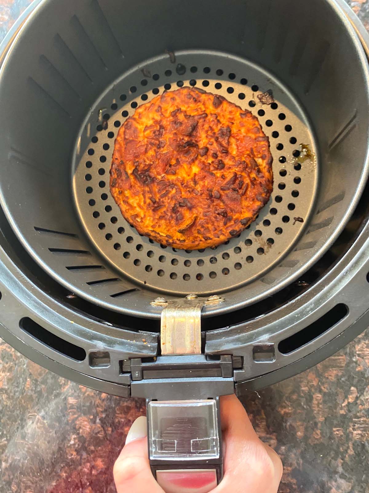 Single size deep dish frozen pizza in air fryer basket being removed from air fryer.