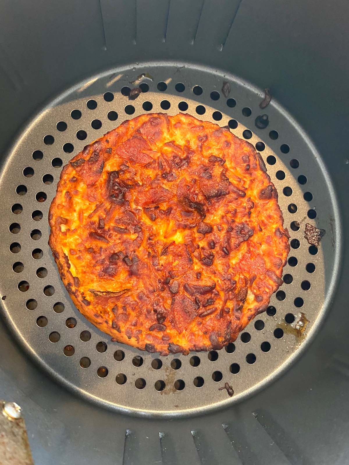 Single size deep dish frozen pizza in air fryer basket after cooking.