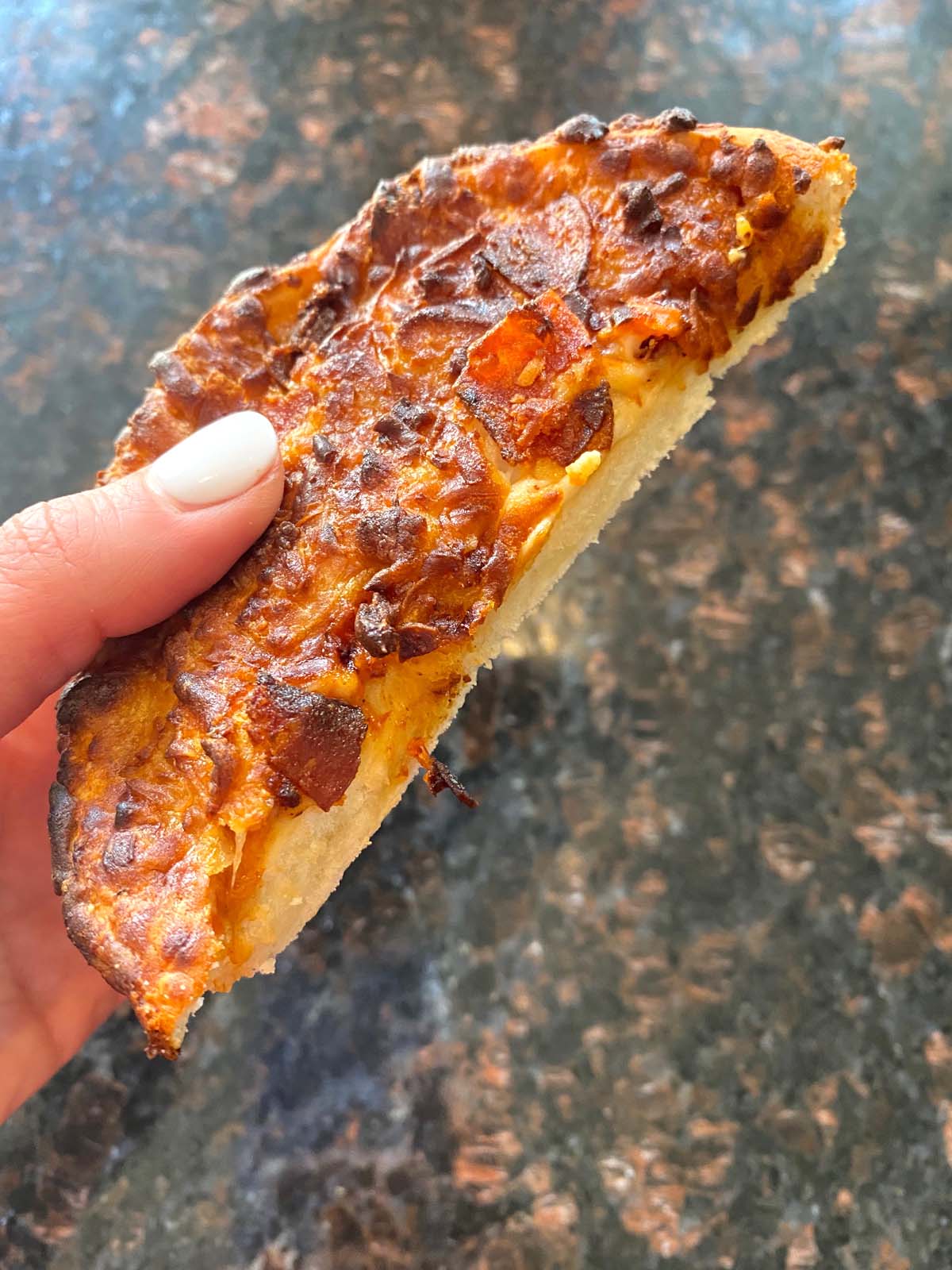 Hand holding half of deep dish pizza showing the inside texture.