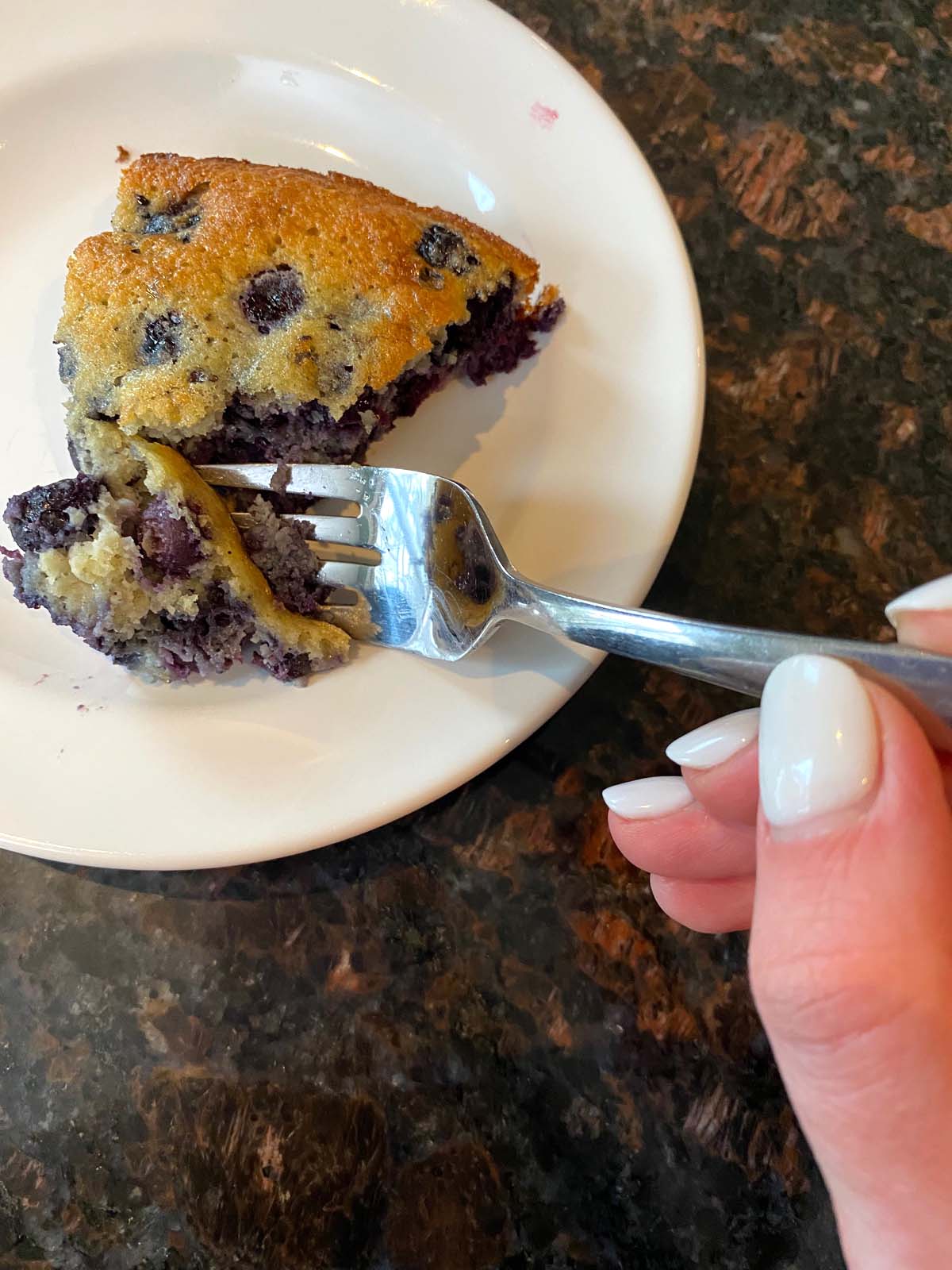A slice of gluten free blueberry cake on a plate with a fork digging into it.