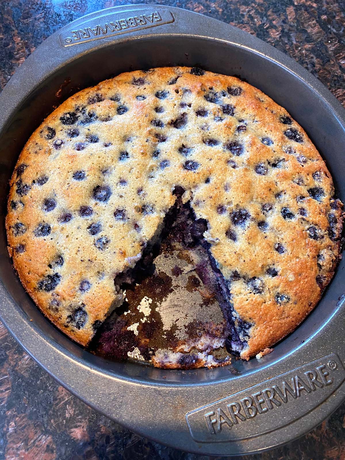 Baked gluten free blueberry cake in the pan with a slice missing.