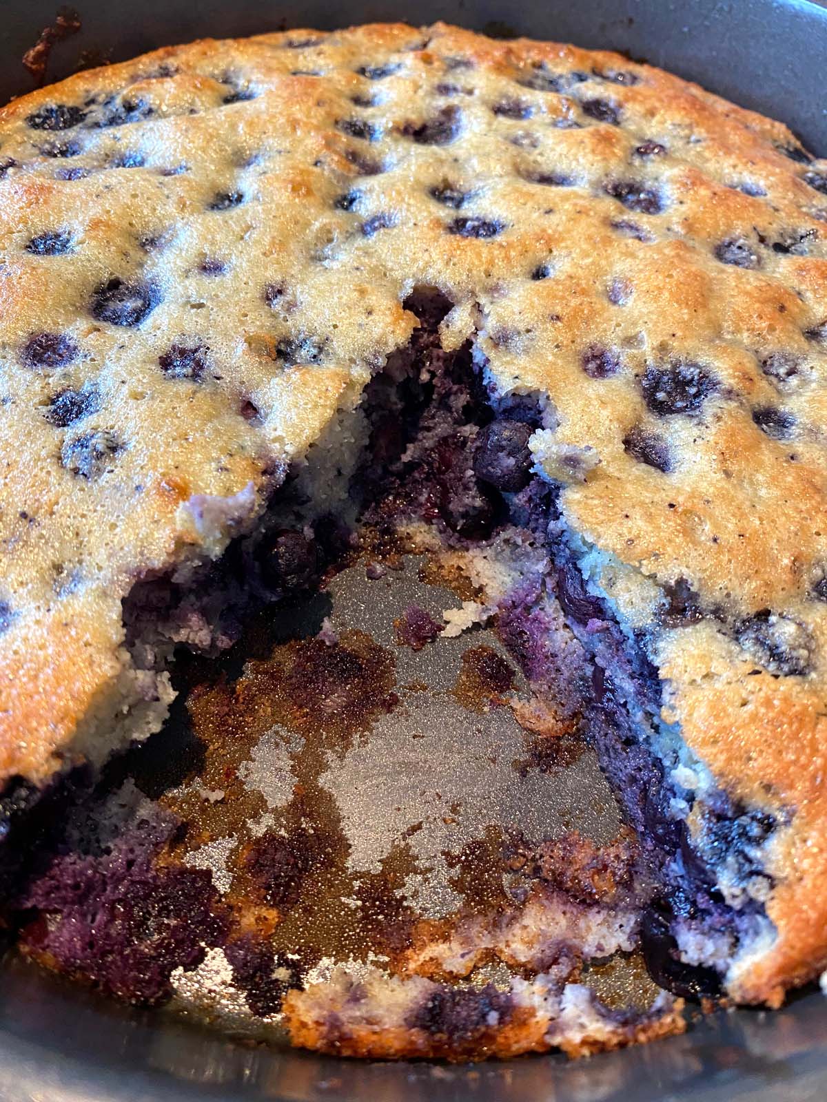 Baked gluten free blueberry cake in the pan with a slice missing.