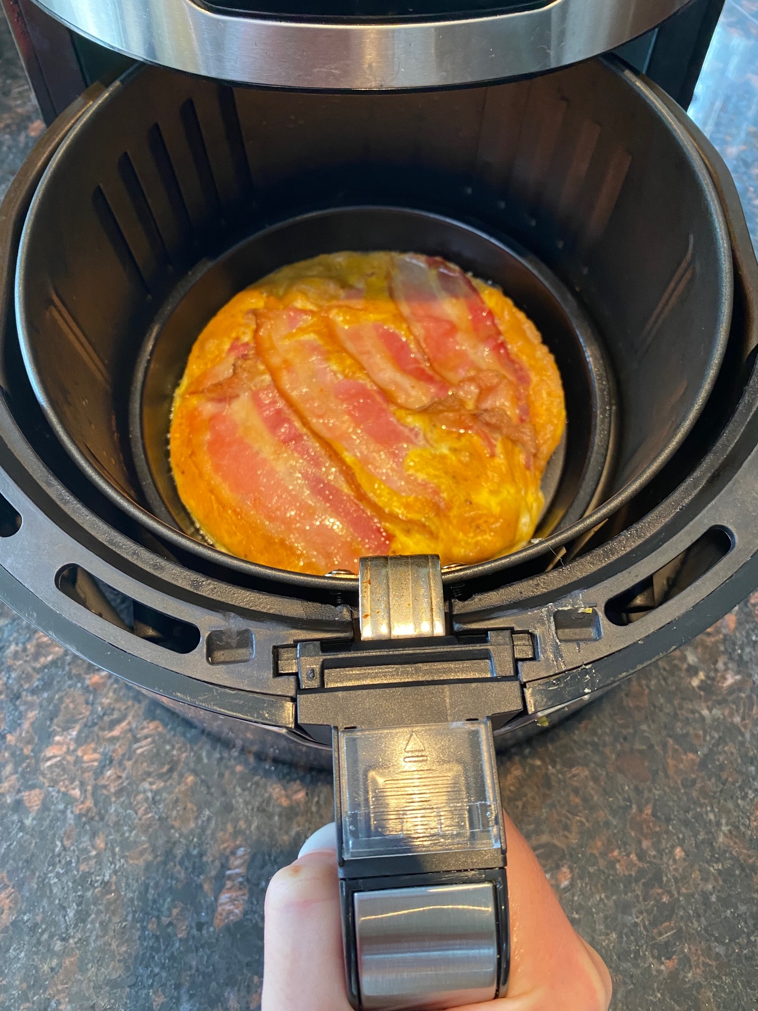 Cooked bacon and eggs in the air fryer basket.